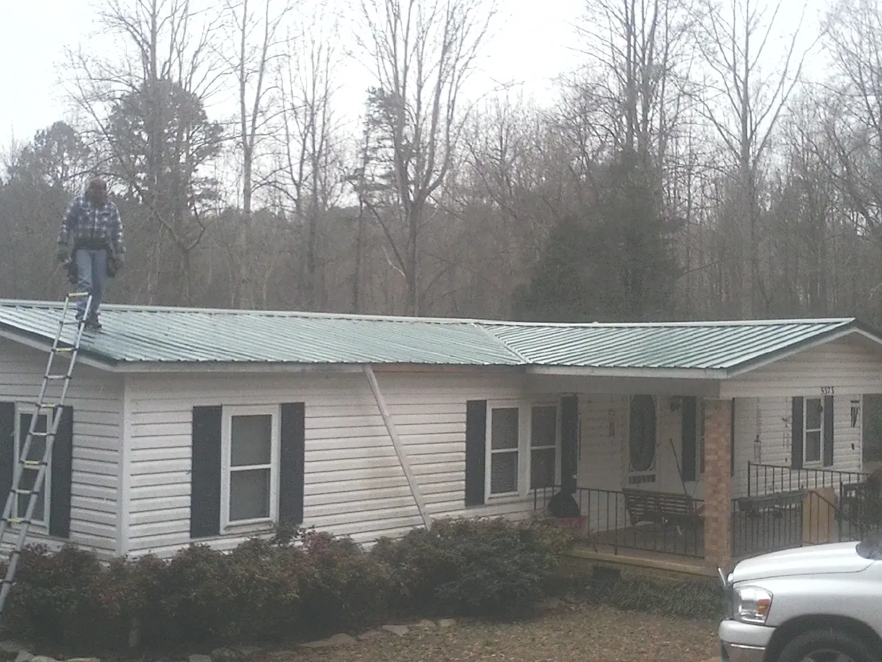 Worker on a ladder beside a new green metal roof on a ranch home in Croton Falls