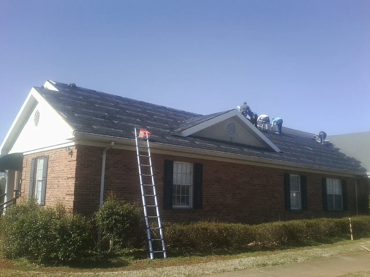 Crew tearing shingles off a brick ranch roof with a ladder set — Emergency Roof Repair work by our crew in Croton Falls