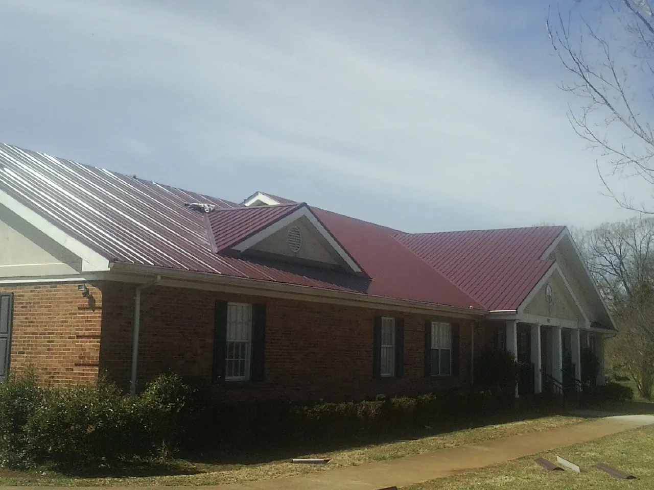 Red metal roof with gabled entries on a long brick building, from a Hail Damage Roof Repair job in Croton Falls