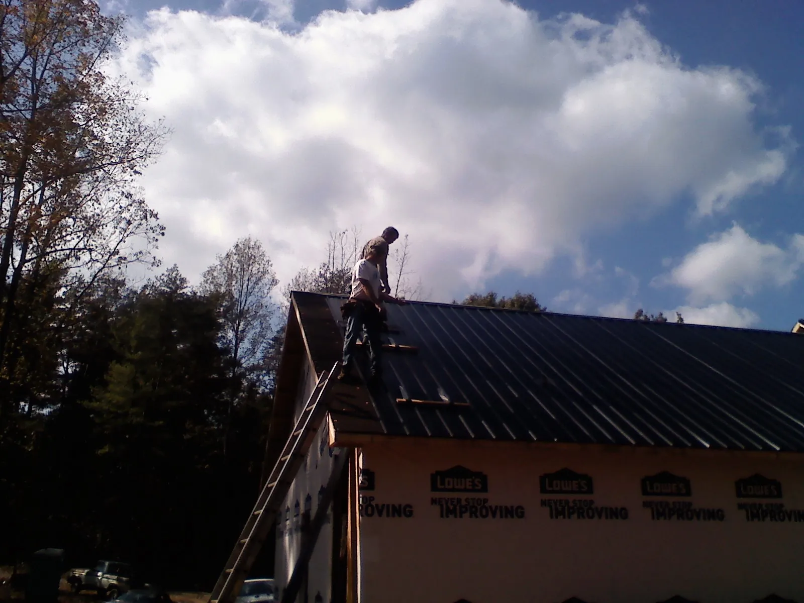 Roofer fastening dark metal panels high against a cloudy sky, from a Roof Inspection job in Croton Falls