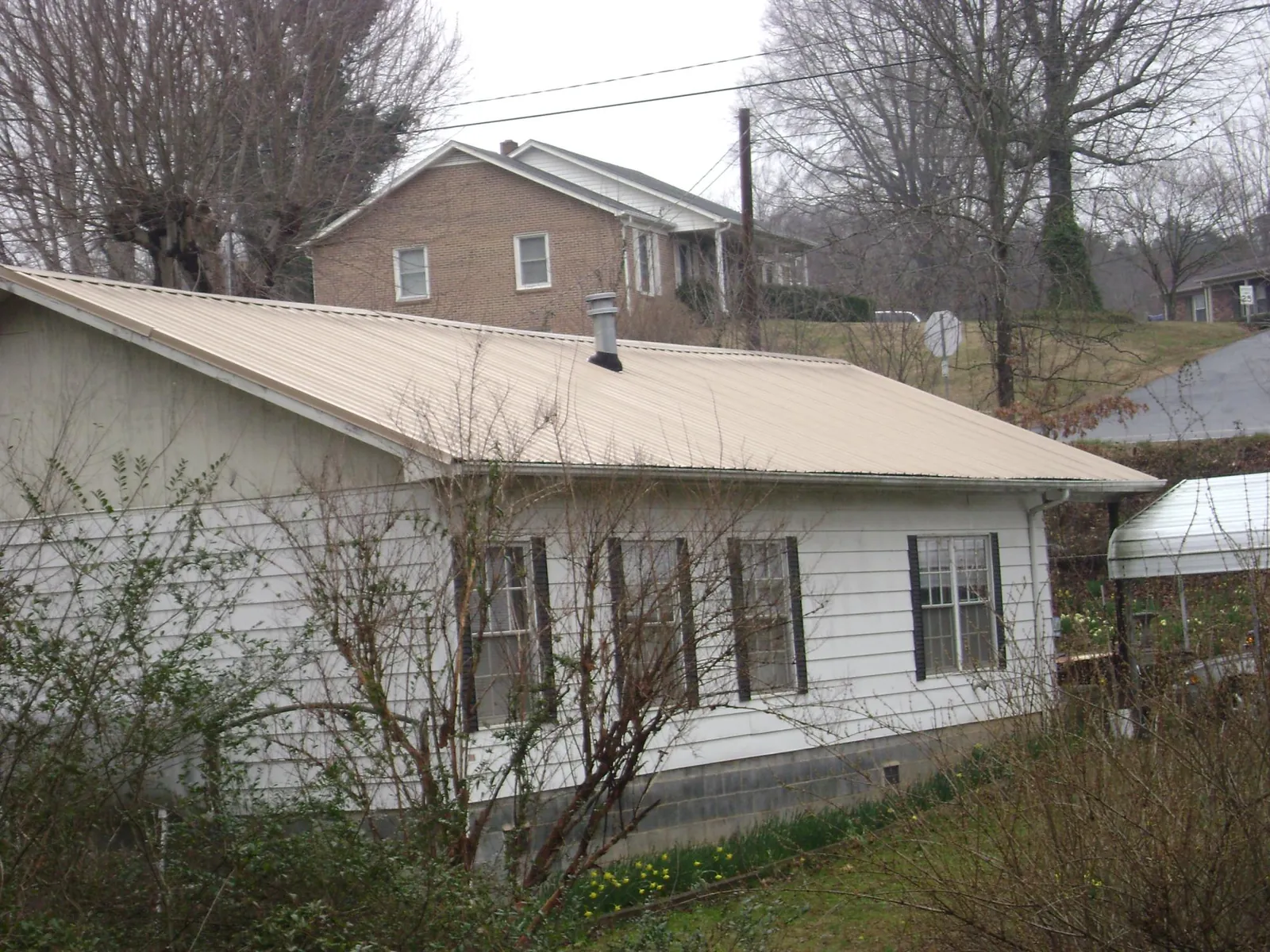 Tan metal roof on a white sided house set into a hillside — Commercial Roofing by Roofing Brothers in Croton Falls