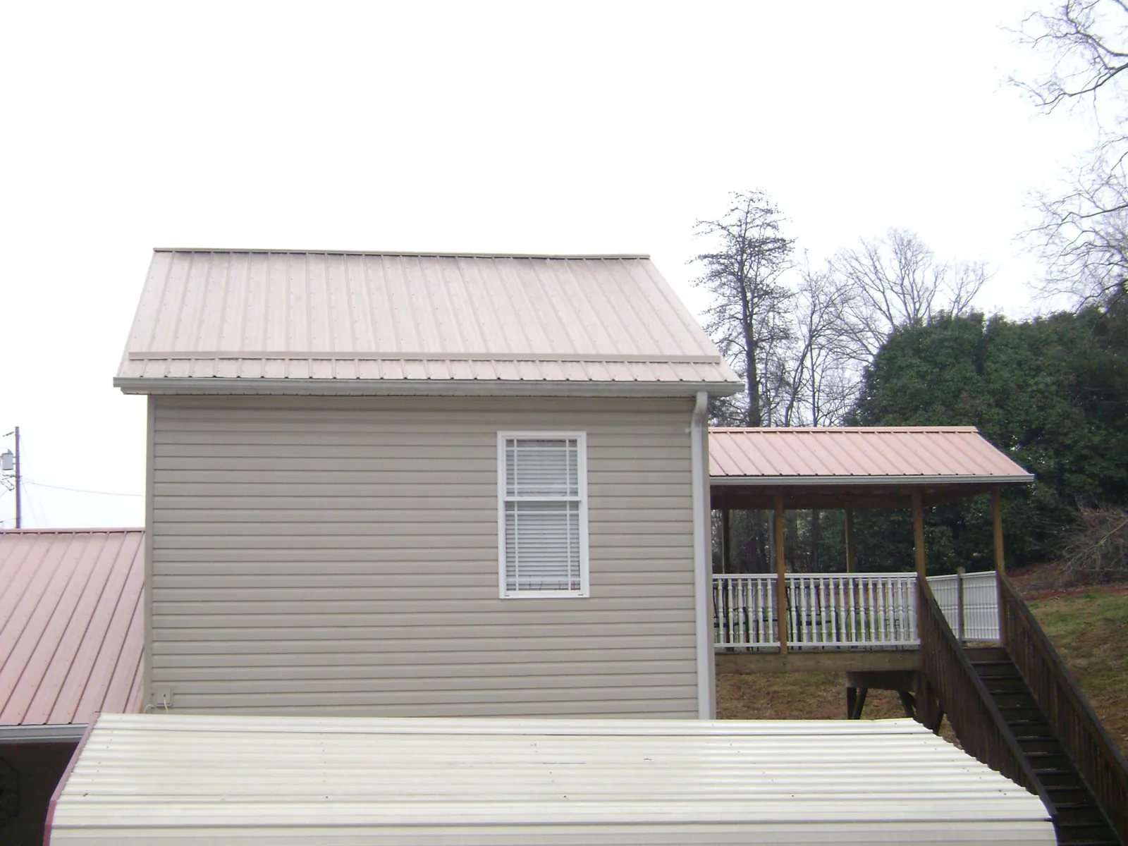 Tan metal roofs on a two story addition and attached porch, from a Roof Replacement job in Croton Falls